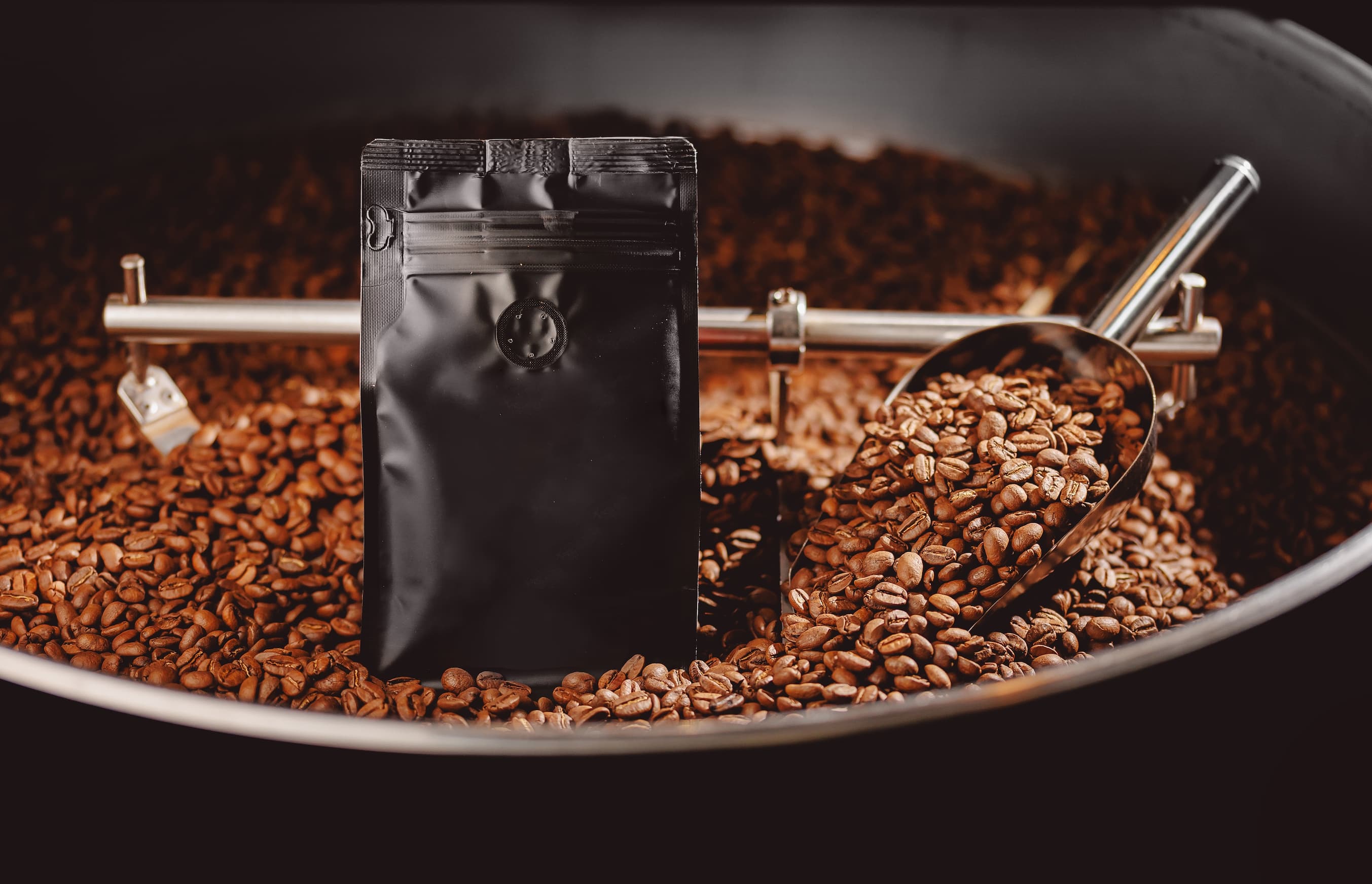 Kaffeeverpackung mit Bohnen Schwarze Kaffeeverpackung steht zwischen frisch gerösteten Kaffeebohnen.