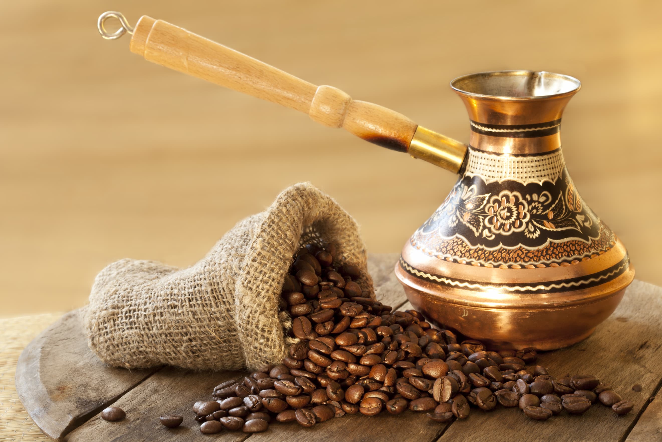 Kaffeebohnen mit traditioneller Kupferkanne Aus einem Jutesack fallende Kaffeebohnen neben traditioneller Kupferkanne auf Holzbrett.