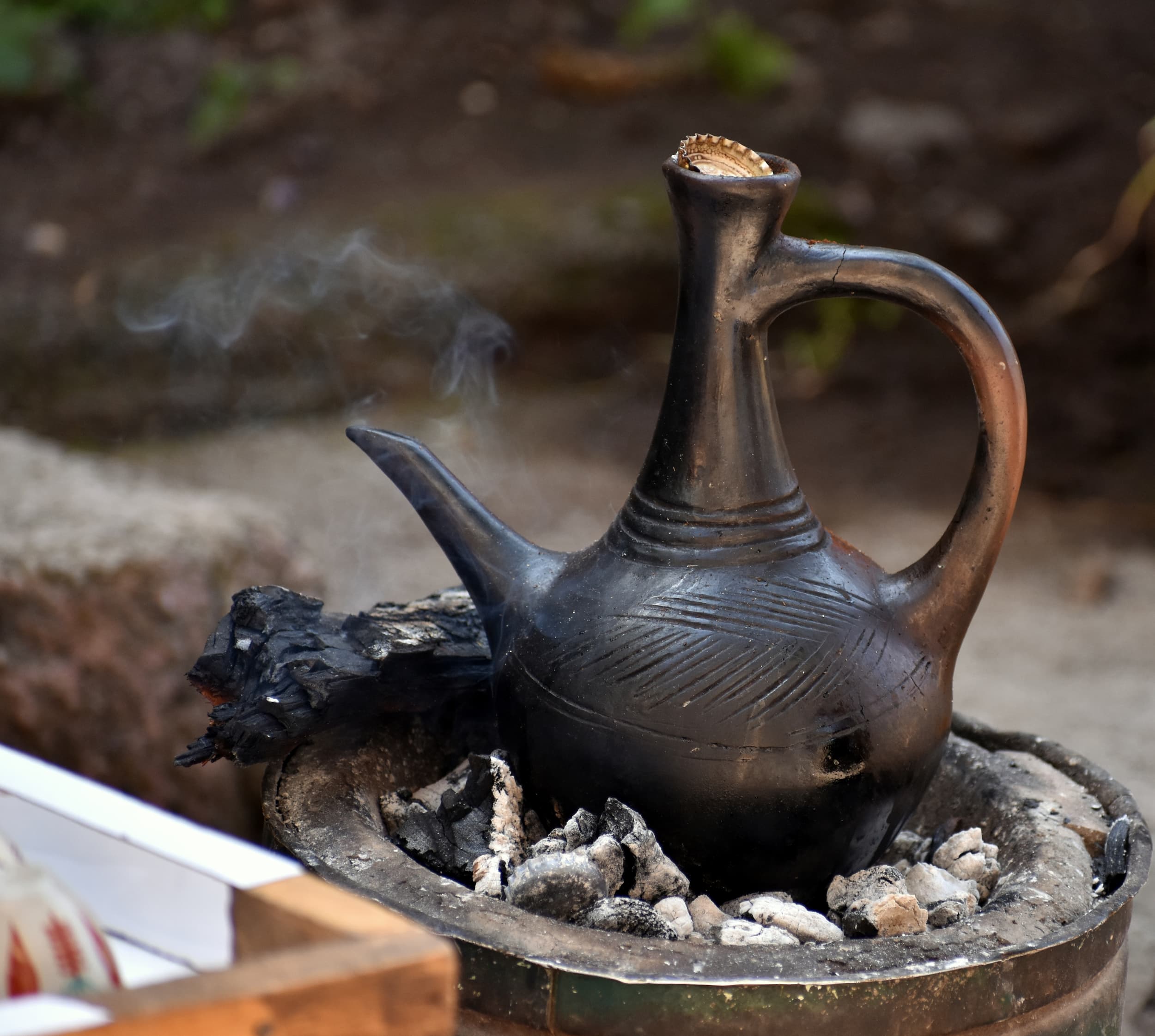 Traditionelle Kaffeekanne auf Holzfeuer Schwarze traditionelle Kaffeekanne aus Ton, die auf gluehenden Kohlen erhitzt wird.