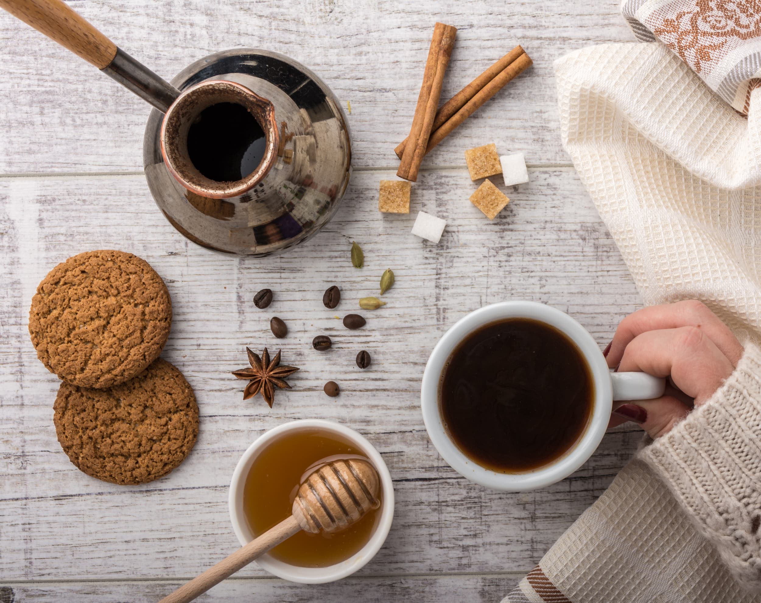 Tasse Kaffee mit Honig, Keksen und winterlichen Gewürzen auf hellem Holztisch.