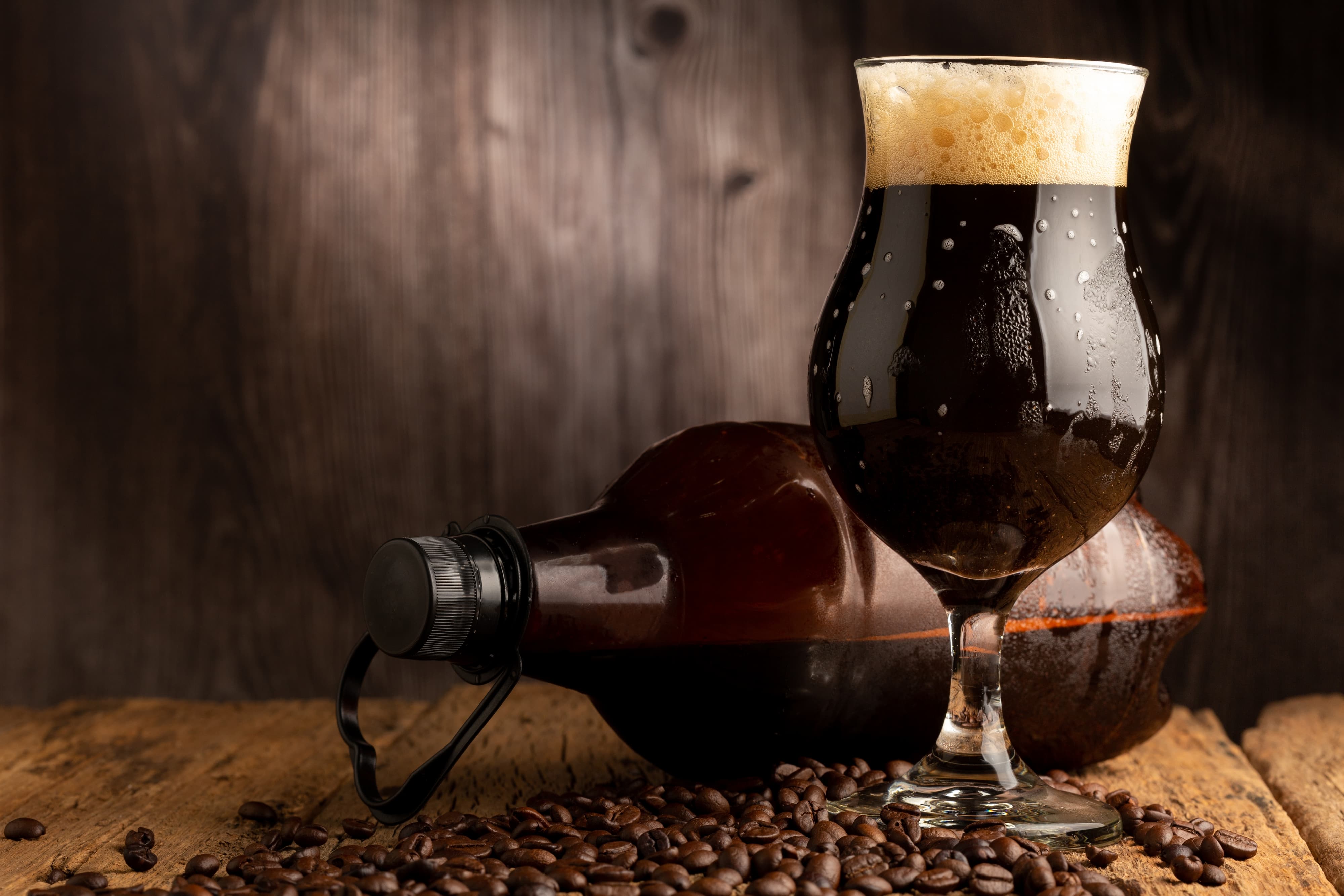 Glas mit dunklem Coffee Stout Bier, daneben Kaffeebohnen auf Holztisch.