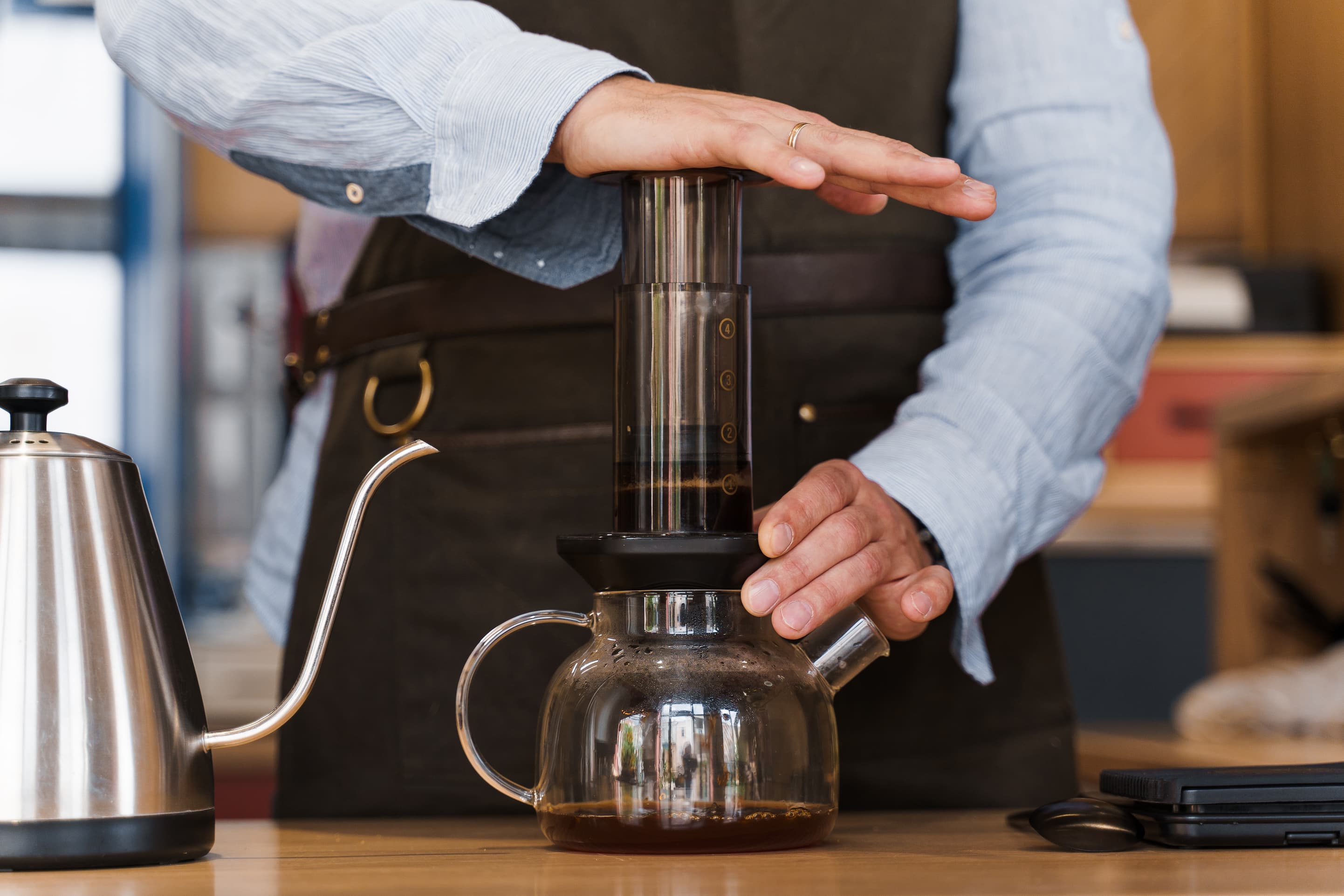 Traditionelle Kaffeezubereitung Barista bereitet Kaffee auf traditioneller Art in Glas-Kanne auf Holztisch zu.