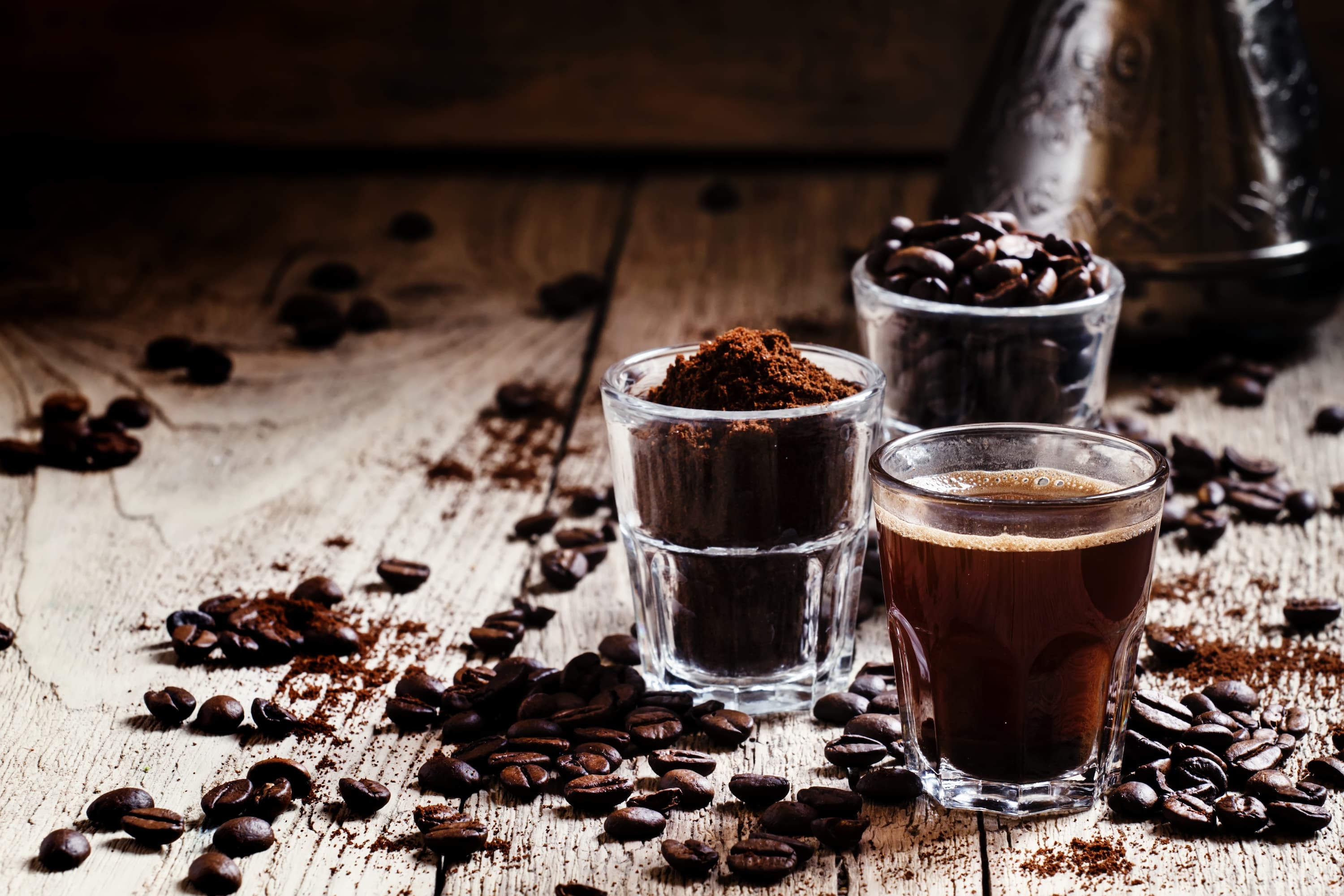 Kaffeebohnen, Kaffeepulver und Espresso im Glas Drei Gläser mit Kaffeebohnen, Kaffeepulver und frischem Espresso auf Holztisch.