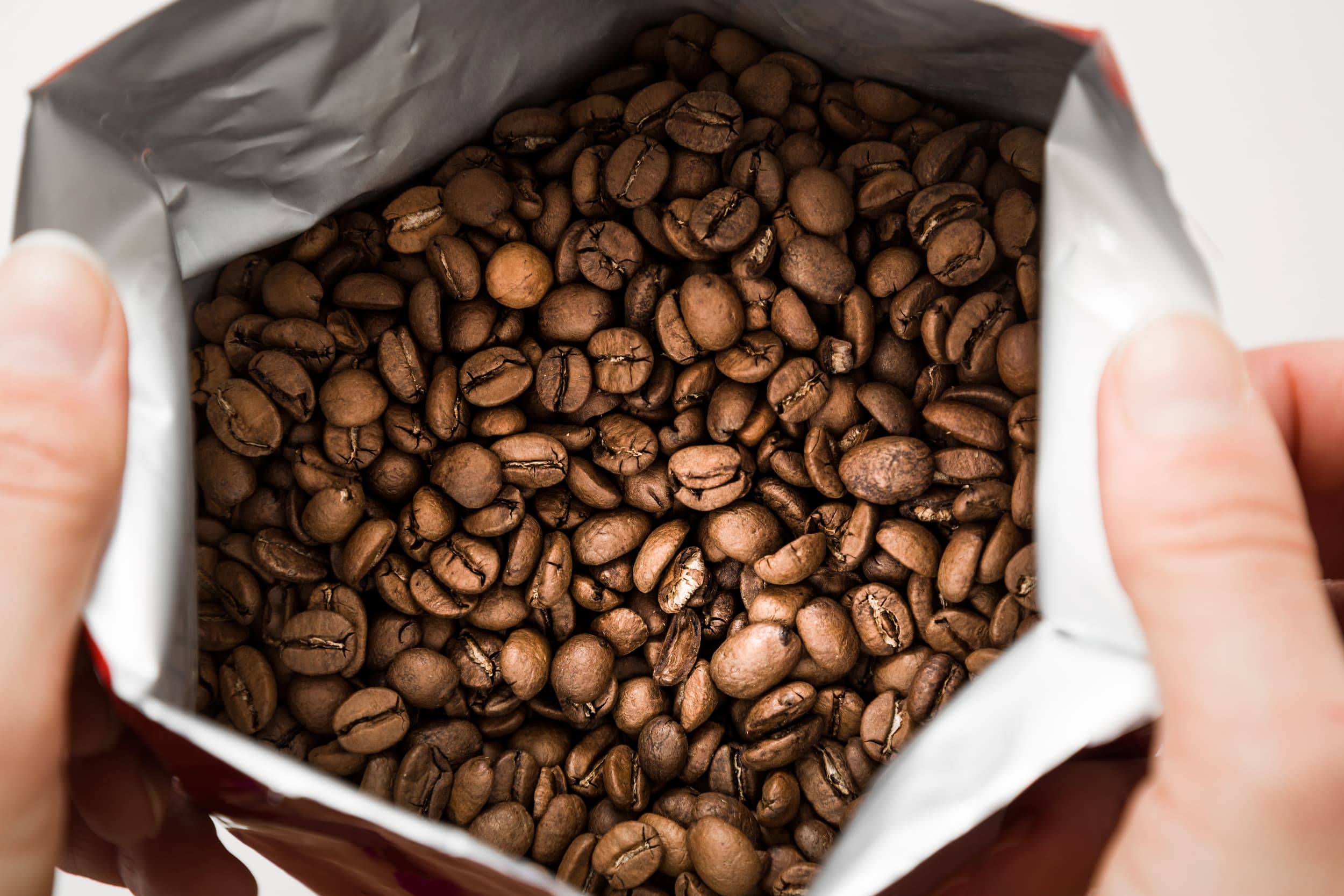 Geöffnete Kaffeeverpackung mit Bohnen Hände öffnen Kaffeeverpackung mit frisch gerösteten Bohnen.