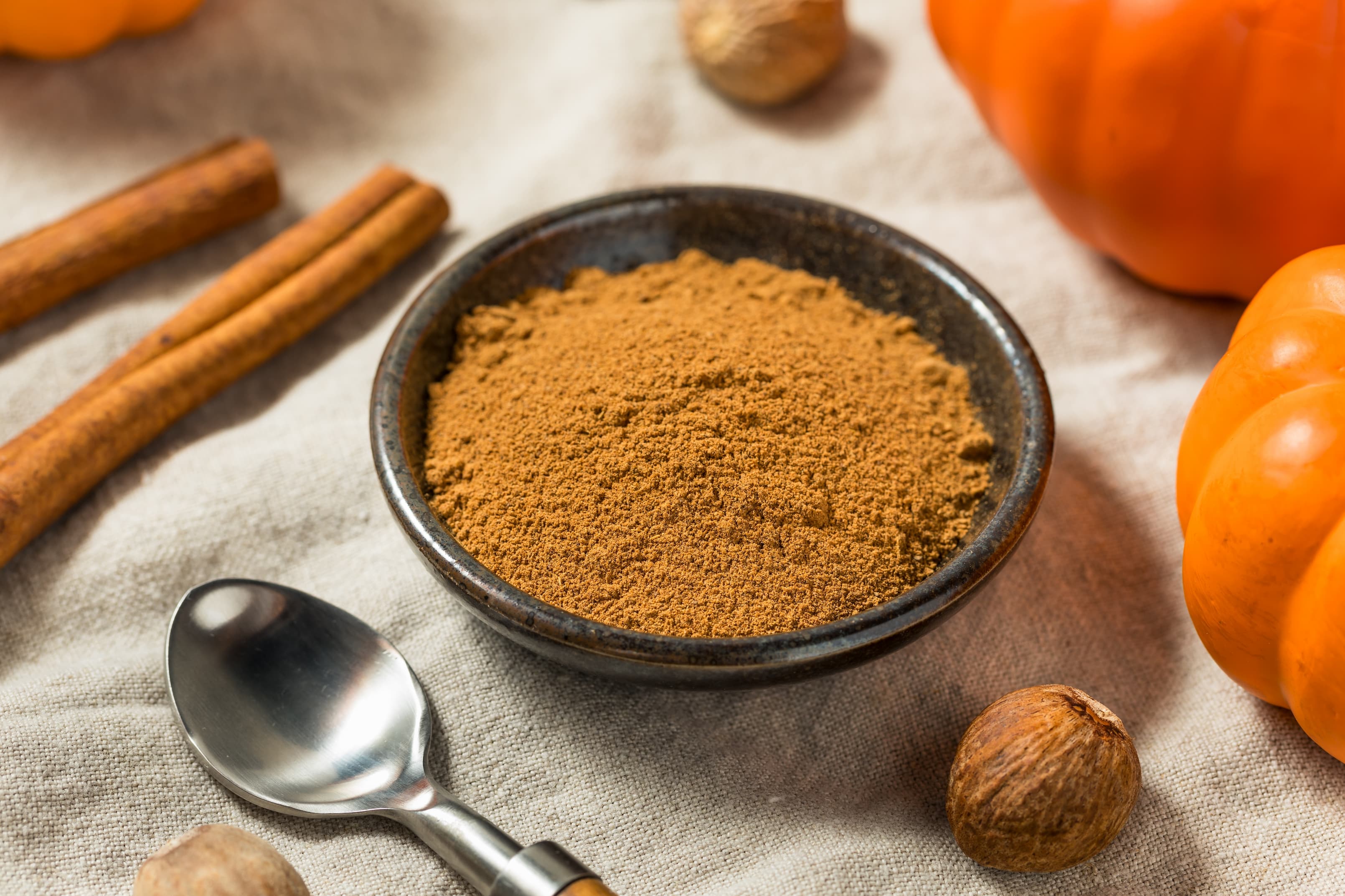 Schale mit gemahlenem Zimt, Zimtstangen und Kürbis als Herbstdeko.