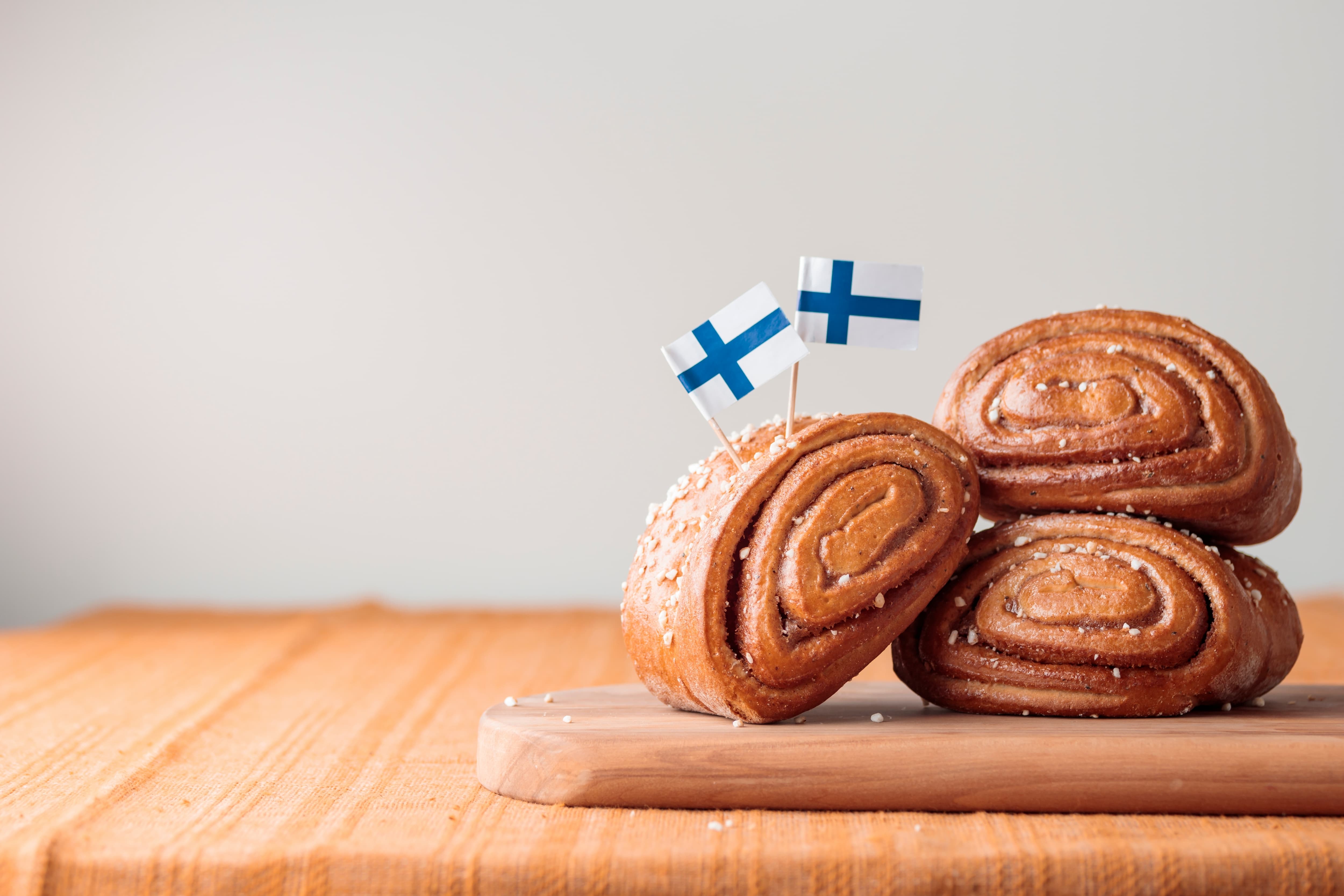 Finnisches Gebäck mit Flagge Zimtschnecken dekoriert mit finnischen Flaggen auf einem Holztisch.