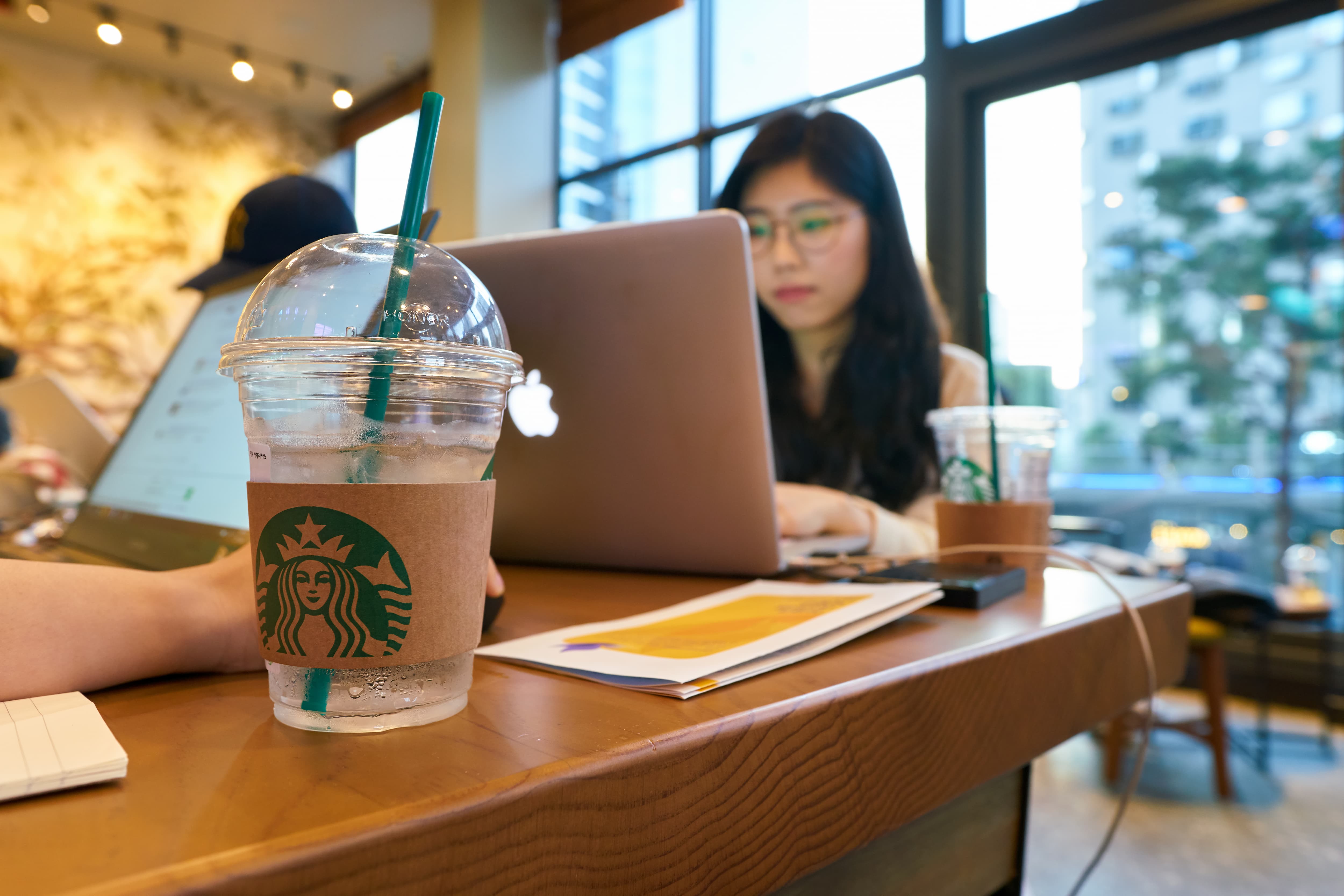 Junge Frau arbeitet am Laptop im Starbucks Café, Getränkebecher im Vordergrund.