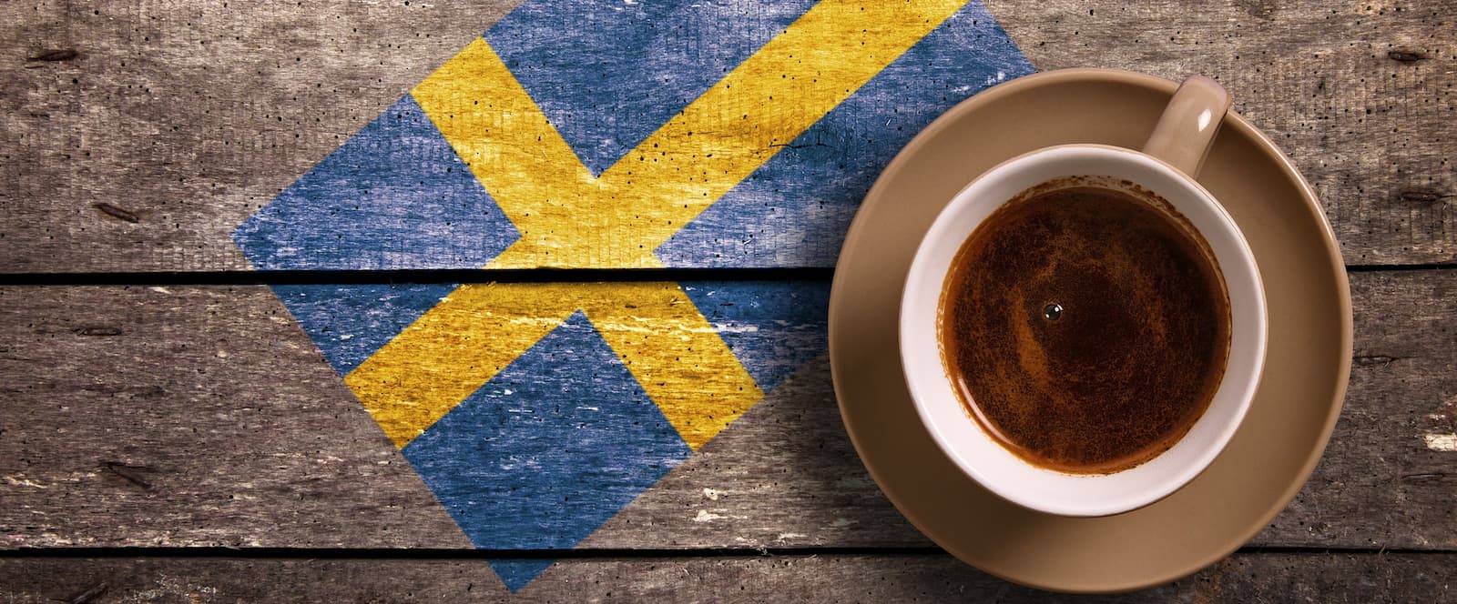 Kaffee mit schwedischer Flagge – Fika Kultur Tasse Kaffee auf Holzuntergrund mit schwedischer Flagge, Symbol für Fika Kaffeekultur.
