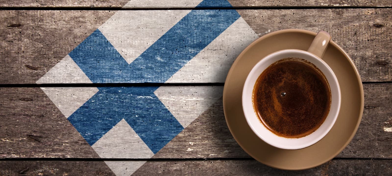Kaffee mit finnischer Flagge Tasse Kaffee auf Holz mit aufgemalter finnischer Flagge – Symbol für Kaffeekultur in Finnland.