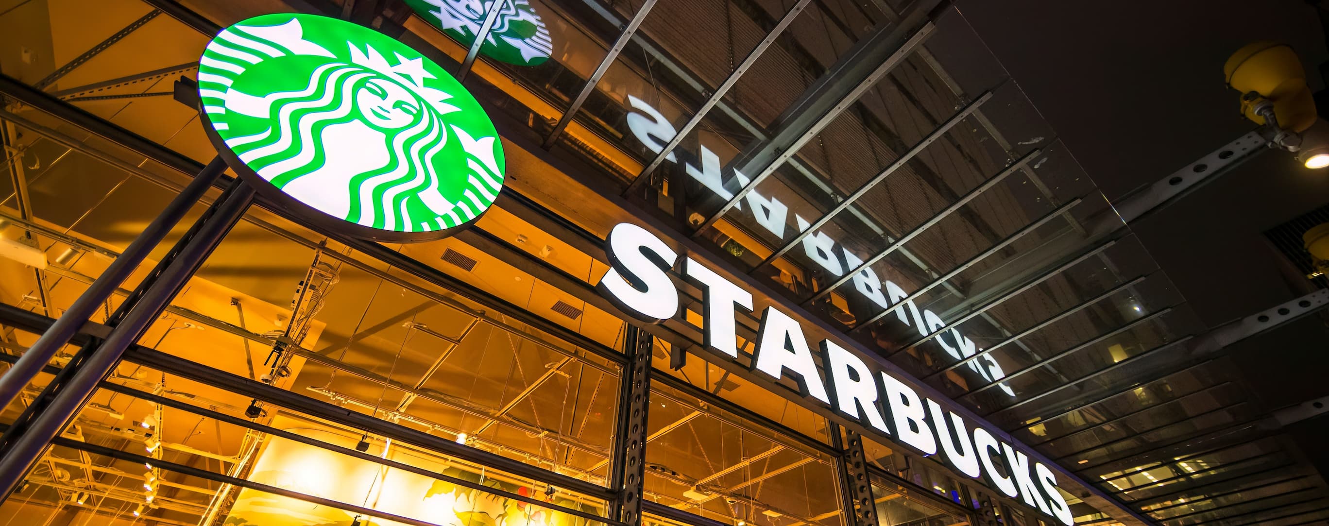Außenansicht einer Starbucks Filiale mit beleuchtetem Logo.