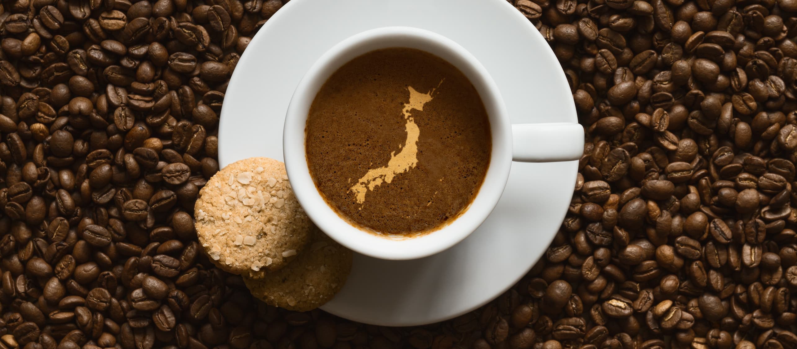 Japan-Silhouette im Kaffee Tasse Kaffee mit Schaum in Form der Japan-Landkarte, umgeben von Kaffeebohnen und Keksen.