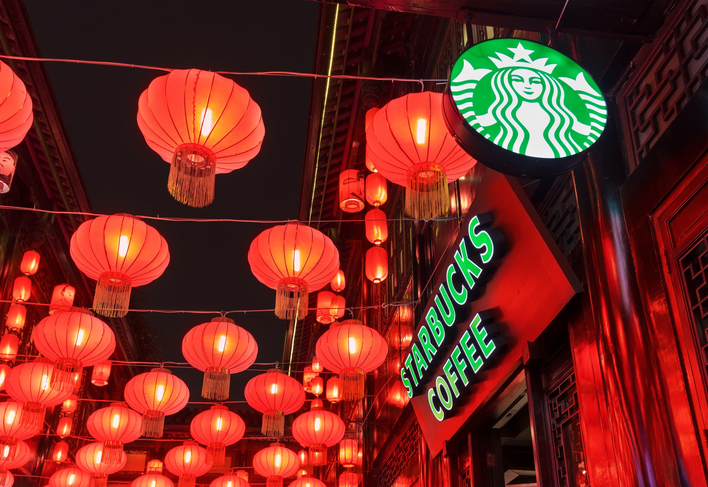 Beleuchtete rote Laternen ueber einem Starbucks Café bei Nacht in asiatischem Stadtviertel.