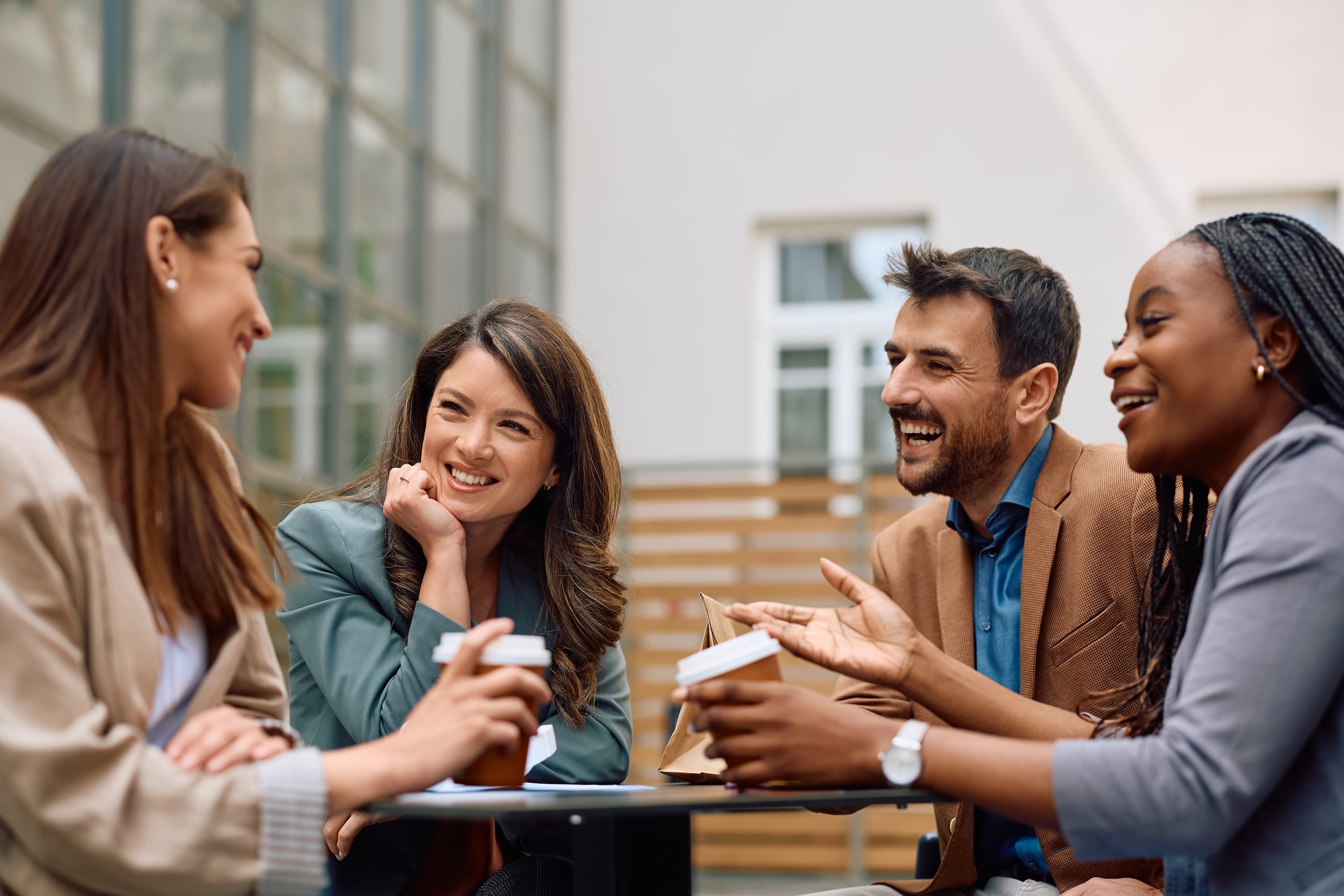 Gruppe von Kollegen genießt Kaffee und unterhält sich lachend im Freien.