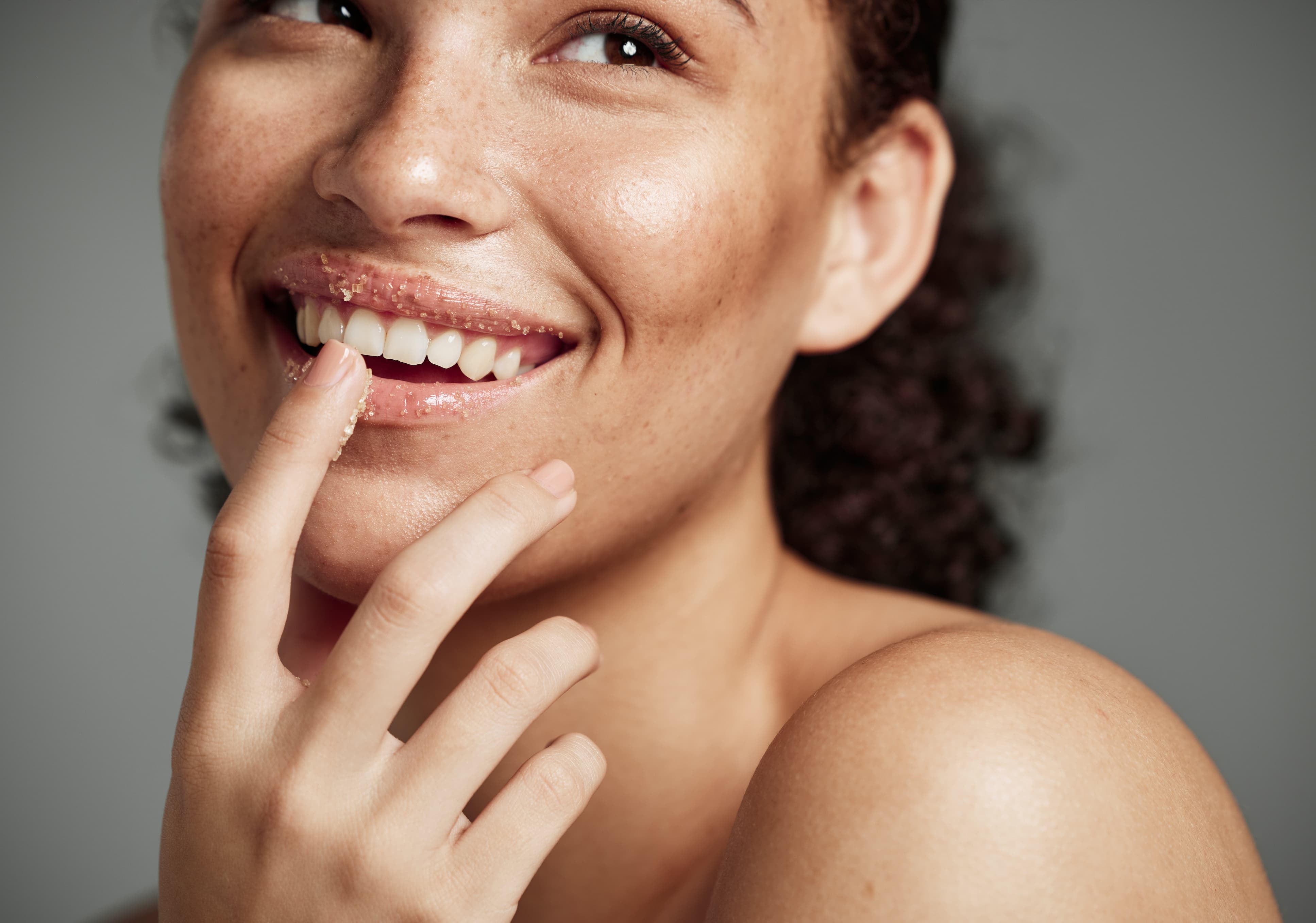 Lippenpeeling mit Kaffee Frau trägt Lippenpeeling mit Kaffeepartikeln auf und lächelt.
