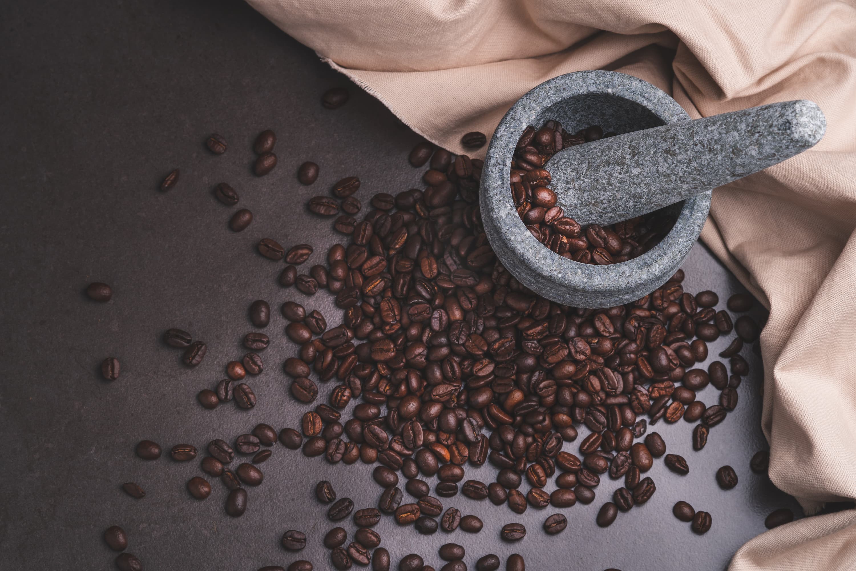 Kaffeebohnen mit Mörser Frische Kaffeebohnen auf dunklem Untergrund mit Moerser und Stoeßel aus Stein.