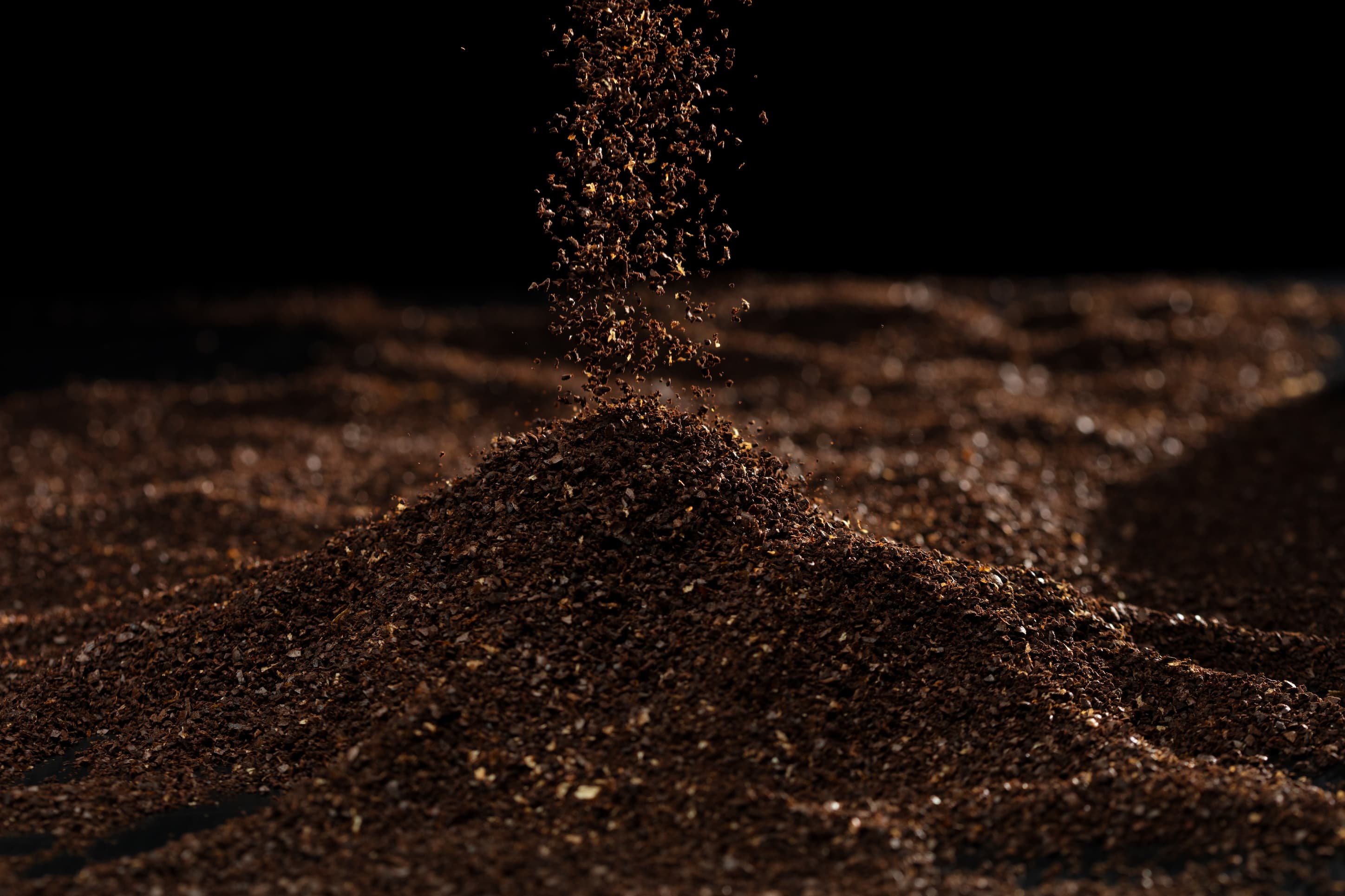 Fein gemahlener Kaffee fällt zu einem Häufchen vor schwarzem Hintergrund.
