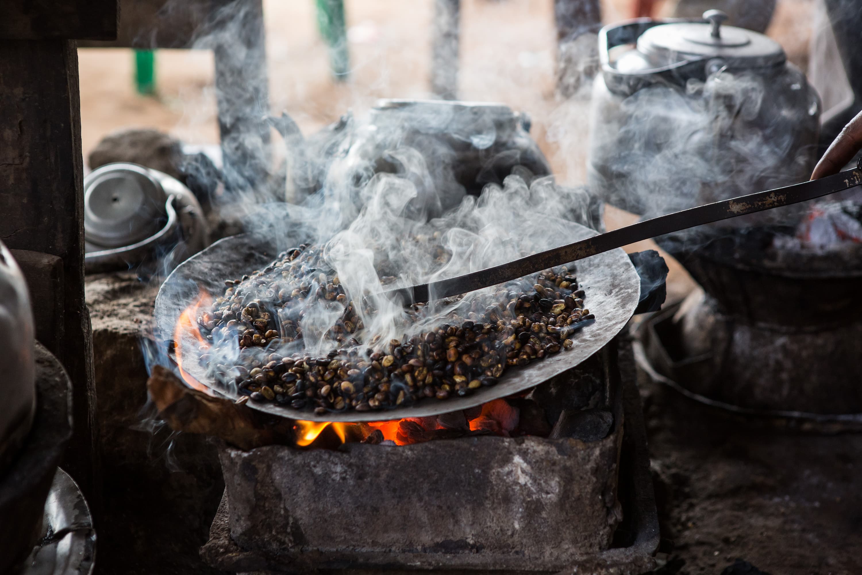 Traditionelle Röstung von Kaffeebohnen über offenem Feuer Frische Kaffeebohnen werden traditionell über Feuer geröstet, Rauch steigt auf.